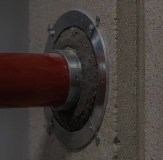 Traversée de mur : tube d'acier peint passant au travers d'une paroi béton, avec sa platine de finition.